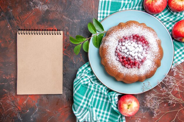 Nahaufnahme von oben ein Kuchen ein Kuchen mit roten Johannisbeeräpfeln auf dem karierten Tischtuch cremefarbenes Notizbuch