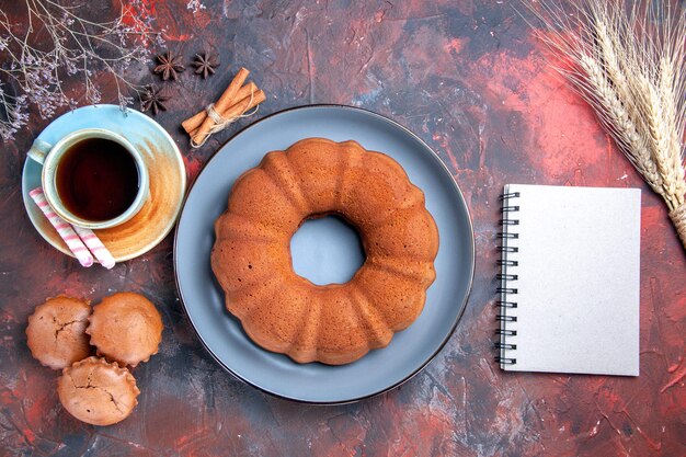 Nahaufnahme von oben ein Kuchen eine Tasse Tee Süßigkeiten ein Kuchen Cupcakes Zimt und Notizbuch