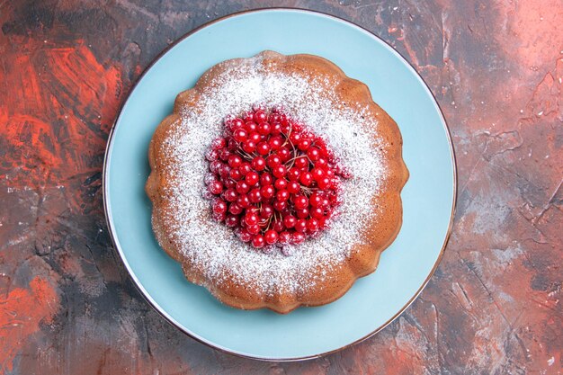 Kostenloses Foto nahaufnahme von oben ein tellerkuchen mit roten johannisbeeren auf dem teller auf dem rot-blauen tisch