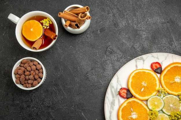 Nahaufnahme von oben eine appetitliche Tasse Tee mit Zitrusfrüchten und Erdbeeren neben den Schalen mit Schokoladen- und Zimtstangen und einer Tasse Tee mit Zitrone