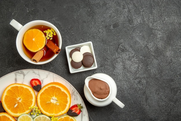 Nahaufnahme von oben eine Tasse Teeteller mit Zitrusfrüchten und Erdbeeren mit Schokoladenüberzug neben den Schalen mit Schokolade und Schokoladencreme und einer Tasse Tee mit Zitronen- und Zimtstangen