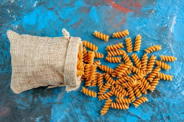 Kostenloses Foto nahaufnahme von roher italienischer pasta aus der grauen handtasche auf der rechten seite auf blauem hintergrund