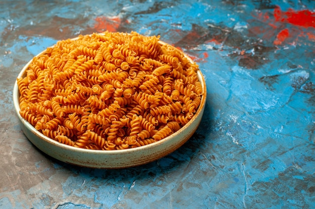 Nahaufnahme von roher italienischer Pasta in einer weißen Schüssel auf blauem Hintergrund