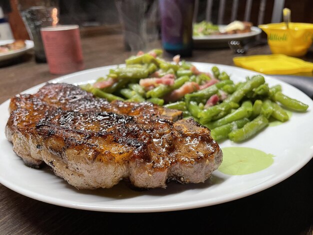 Nahaufnahme von saftigem Fleisch mit grünem Bohnensalat auf einem weißen Teller