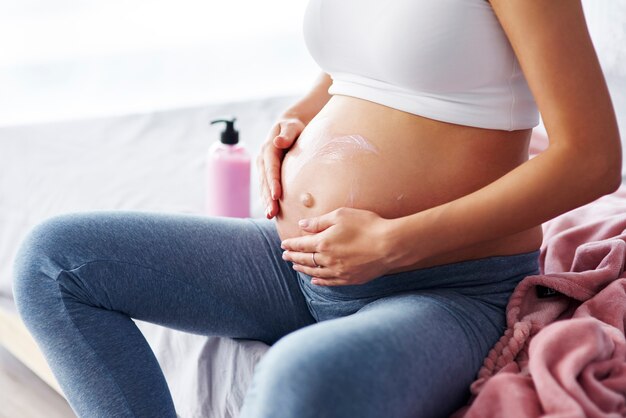 Nahaufnahme von schwangeren Frauen, die Feuchtigkeitscreme auftragen