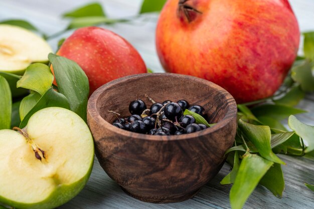 Nahaufnahme von Schwarzdornbeeren in der Schüssel mit ganzem und halb geschnittenem Apfel mit Granatapfel und Blättern