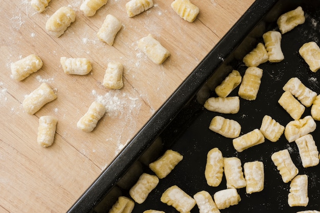 Nahaufnahme von ungekochten selbst gemachten Kartoffelgnocchiteigwaren auf Backblech und -schreibtisch