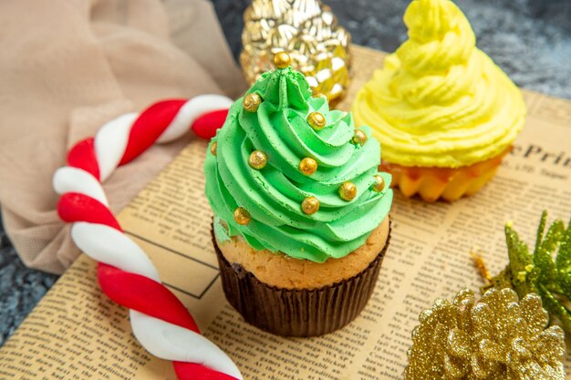 Nahaufnahme von unten Mini Cupcakes Weihnachtssüßigkeiten Weihnachtsornamente auf Zeitungs beige Schal auf Dunkelheit