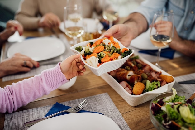 Nahaufnahme von vater und kind, die salat beim mittagessen am esstisch passieren