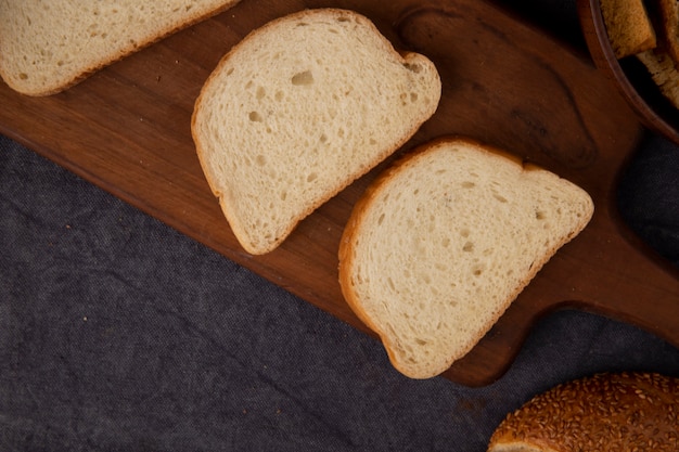 Nahaufnahme von Weißbrotscheiben auf Schneidebrett auf kastanienbraunem Hintergrund mit Kopienraum