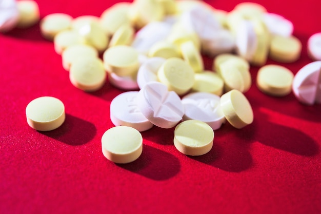 Nahaufnahme von weißen und gelben Pillen auf rotem Hintergrund