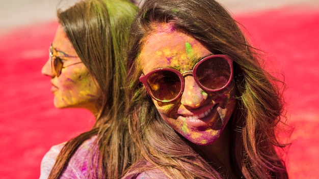 Nahaufnahme von zwei Frauen, welche die Sonnenbrille bedeckt mit holi Farbpulver tragen