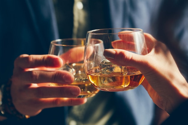 Nahaufnahme von zwei Personen, die bei einem Toast Gläser mit Alkohol klingeln