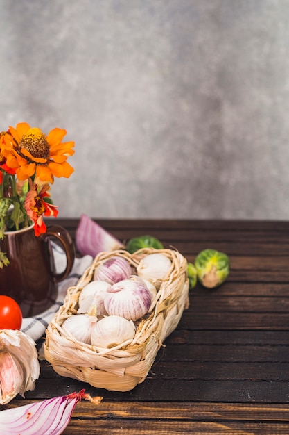 Nahaufnahme von Zwiebeln; Rosenkohl; Knoblauchzehen; Blumen und Stoff auf Holzoberfläche