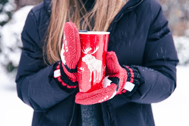 Nahaufnahme weiblicher Hände in Kanada-Handschuhen halten eine rote Thermotasse
