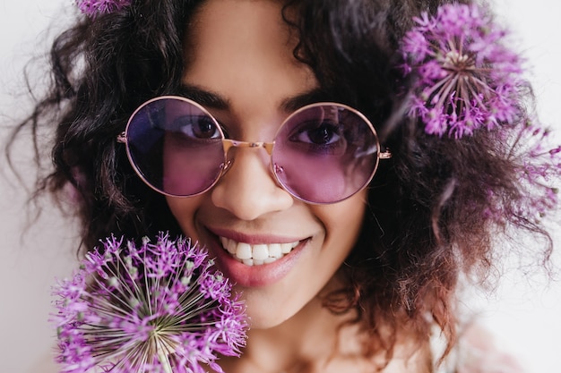 Nahaufnahmeaufnahme der ekstatischen afrikanischen Frau mit Allium. Porträt des lockigen schwarzen Mädchens, das Glück ausdrückt.