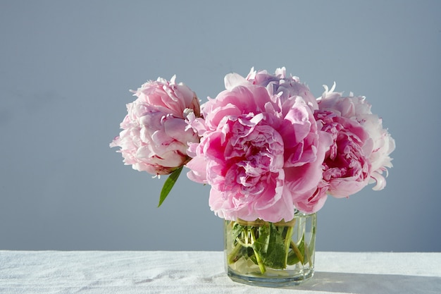 Kostenloses Foto nahaufnahmeaufnahme der herrlichen rosa pfingstrosen in einem kurzen glas auf grauem tisch