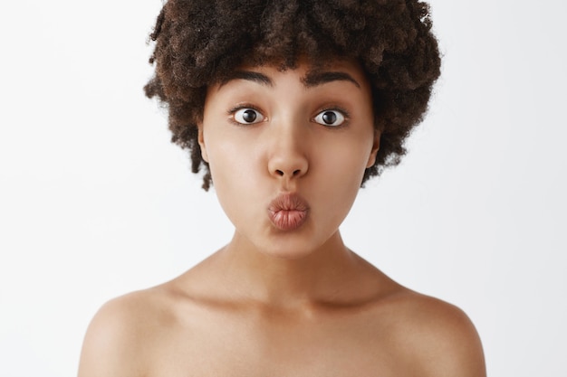 Nahaufnahmeaufnahme der zarten und sanften nackten Frau mit Afro-Frisur, die Lippen faltet und auf leidenschaftlichen Kuss oder Mwah wartet