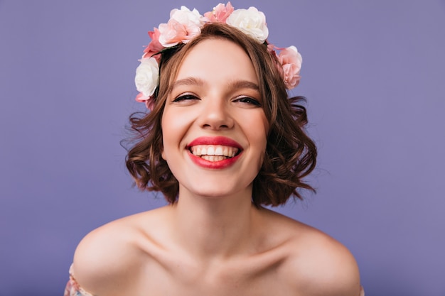 Nahaufnahmeaufnahme des fröhlichen weißen Mädchens mit rosa Blumen im Haar. Emotionale kaukasische Dame lächelnd.