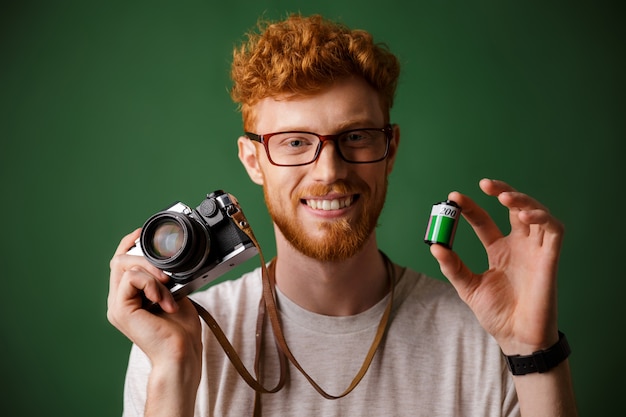 Nahaufnahmeaufnahme des jungen bärtigen hipsters des lesekopfes, der retro-fotokamera und kamerarolle hält