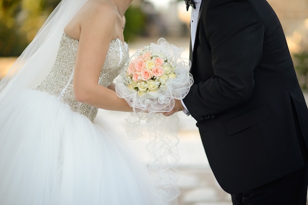 Nahaufnahmeaufnahme einer Braut und eines Bräutigams, die sich küssen, während sie den schönen Blumenstrauß halten