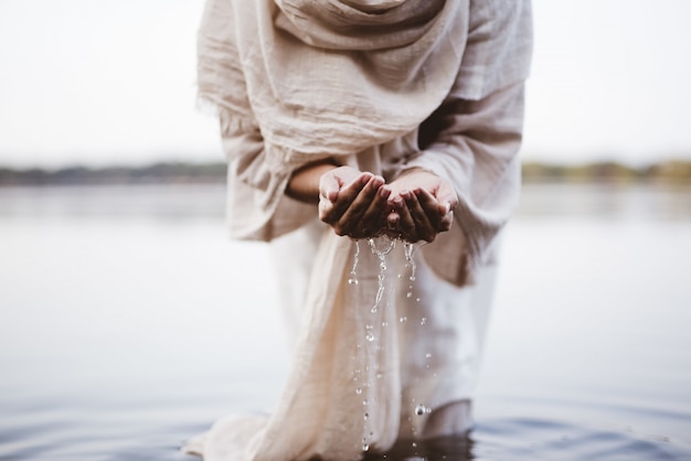 Kostenloses Foto nahaufnahmeaufnahme einer frau, die ein biblisches gewand trägt, das wasser mit ihren handflächen hält