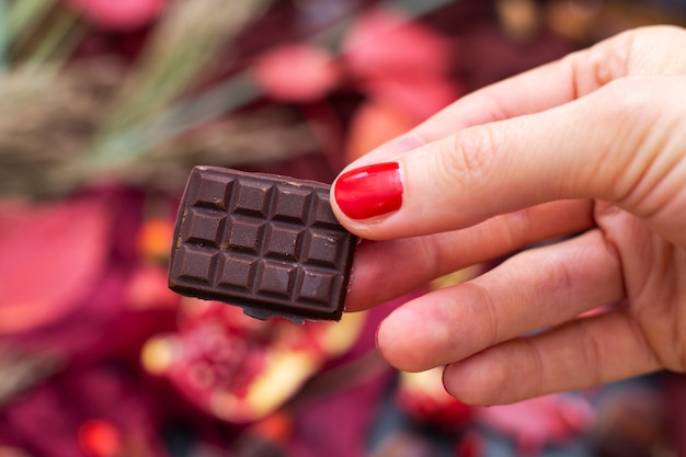 Nahaufnahmeaufnahme einer Frau, die ein Stück rohe vegane Schokolade mit einem unscharfen Hintergrund hält