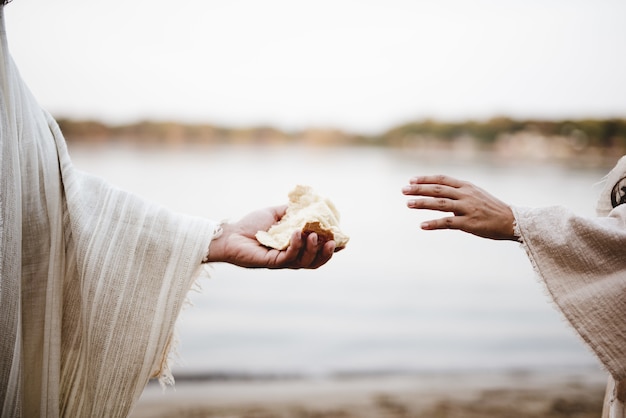 Nahaufnahmeaufnahme einer Person, die ein biblisches Gewand trägt, das einer anderen Person Brot gibt