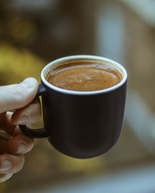 Nahaufnahmeaufnahme einer Person, die eine schwarze Tasse Kaffee hält