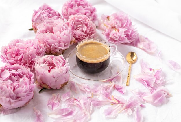 Nahaufnahmeaufnahme einer Tasse Instantkaffee auf einer Untertasse auf dem Tisch mit rosa Pfingstrosen darauf