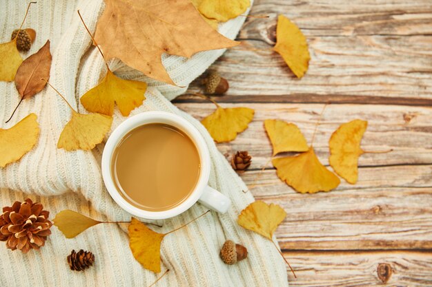 Nahaufnahmeaufnahme einer Tasse Kaffee und Herbstlaub auf hölzernem Hintergrund