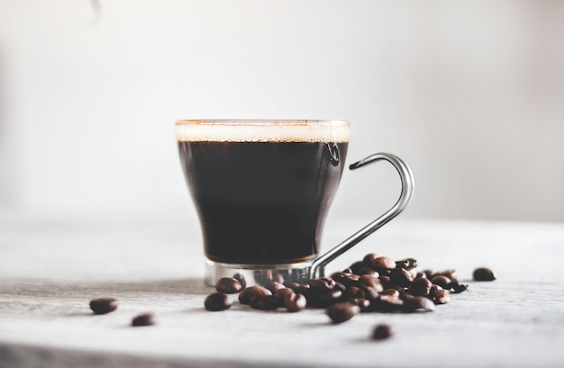 Nahaufnahmeaufnahme einer Tasse schwarzen Kaffees auf dem Tisch mit gerösteten Bohnen unter den Lichtern