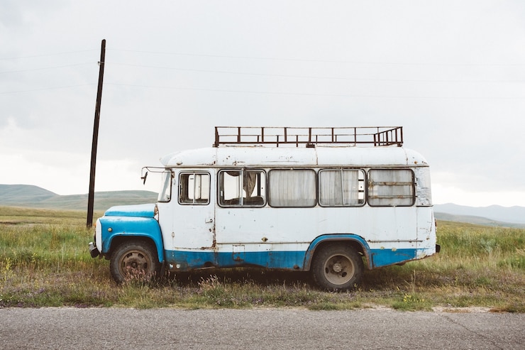 Kostenlose Foto nahaufnahmeaufnahme eines alten kleinbusses auf einer grünen landschaft unter einem bewölkten himmel