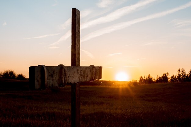 Nahaufnahmeaufnahme eines handgemachten hölzernen Kreuzes in einem Grasfeld mit der Sonne, die im Hintergrund scheint