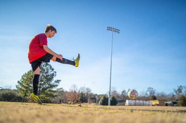 Nahaufnahmeaufnahme eines Jungen, der Fußball auf dem Feld in einer roten Uniform spielt