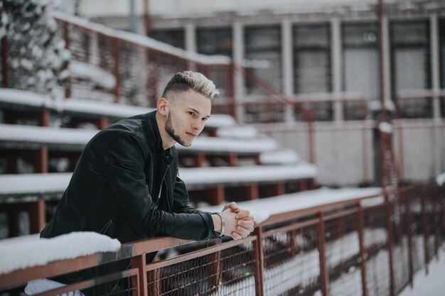 Nahaufnahmeaufnahme eines kaukasischen modischen sexy Mannes, der sich auf einer verschneiten Straße auf den Zaun lehnt