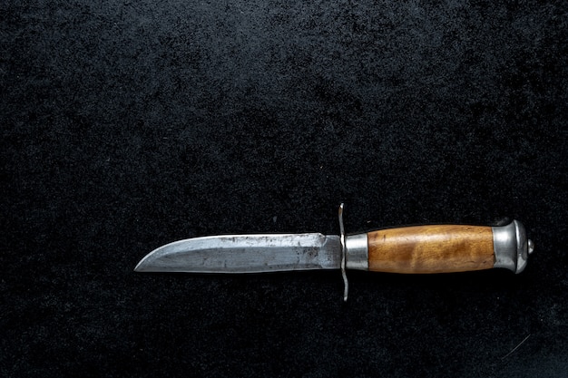 Nahaufnahmeaufnahme eines kleinen scharfen Messers mit einem braunen Griff auf einem schwarzen Hintergrund