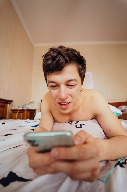 Nahaufnahmeaufnahme eines lässigen Kerls, der im Bett liegt und im Internet surft. Mann mit Smartphone innen.