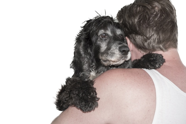 Nahaufnahmeaufnahme eines Mannes, der einen schwarzen Hund hinter auf Weiß umarmt