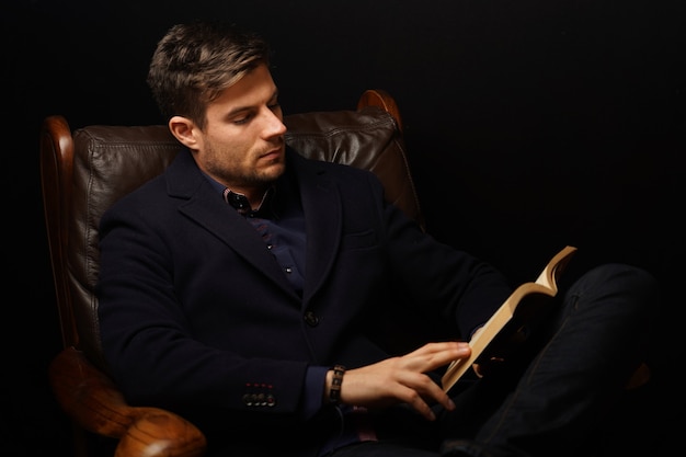 Nahaufnahmeaufnahme eines reifen Mannes im eleganten Anzug, der auf einer Ledercouch sitzt und Buch liest