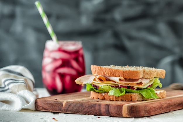 Nahaufnahmeaufnahme eines Sandwiches auf einem hölzernen Nahrungsmitteltablett mit einem gesunden Fruchtshake