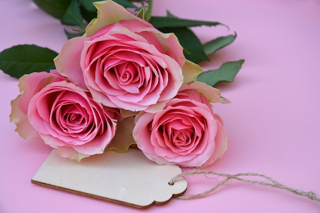 Nahaufnahmeaufnahme von rosa Rosenblumen und einem Etikett mit Platz für Text auf einer rosa Oberfläche