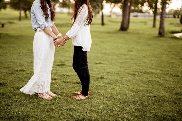 Kostenloses Foto nahaufnahmeaufnahme von zwei frauen, die hände halten, während sie in einem grasfeld mit unschärfe stehen