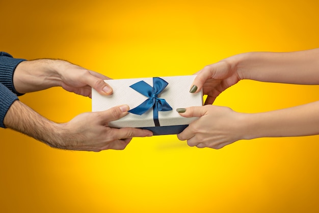 Nahaufnahmebild der Hände des Mannes und der Frau mit Geschenkbox auf gelbem Hintergrund
