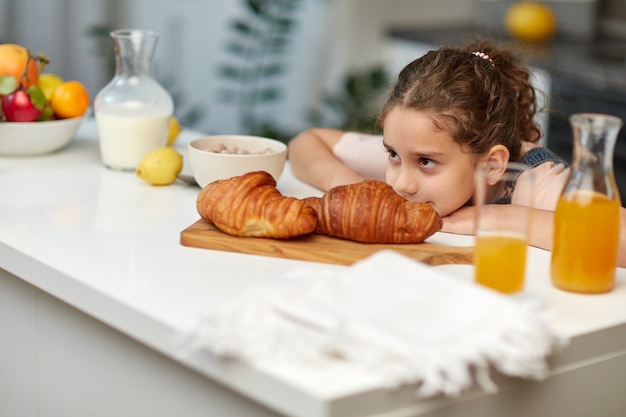 Nahaufnahmebild eines kleinen gelockten mädchens möchte croissant in der küche nehmen.