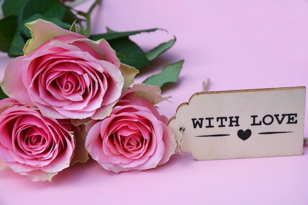 Nahaufnahmebild von rosa Rosen neben der Holzdekoration vor einem rosa Hintergrund