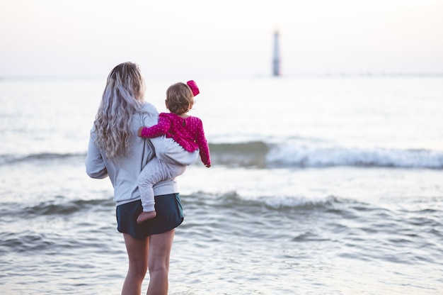 Nahaufnahmefokus schoss von hinten von einer Mutter und ihrem Kind, die das Meer betrachten
