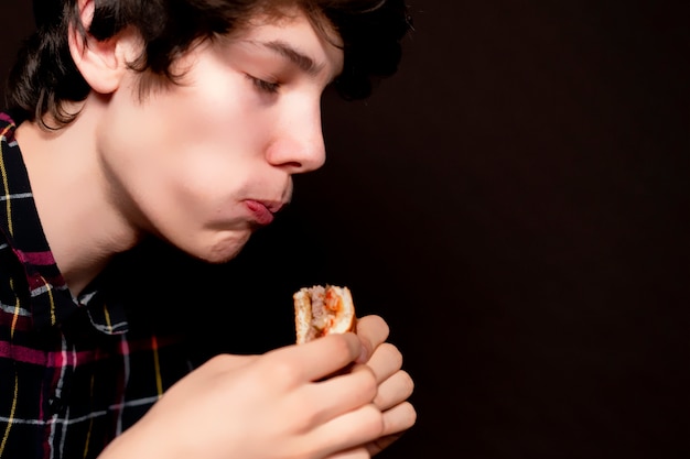 Nahaufnahmefoto des jungen mannes kauen junk-food auf dunklem hintergrund b
