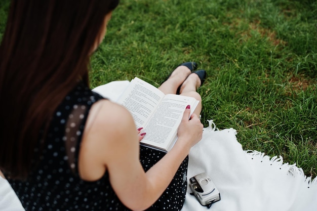 Nahaufnahmefoto des Rückens der Frau, während sie auf der Decke im Gras sitzt und ein Buch liest