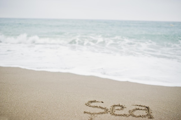 Nahaufnahmefoto des Sandaufschriftmeeres durch die schäumenden Wellen